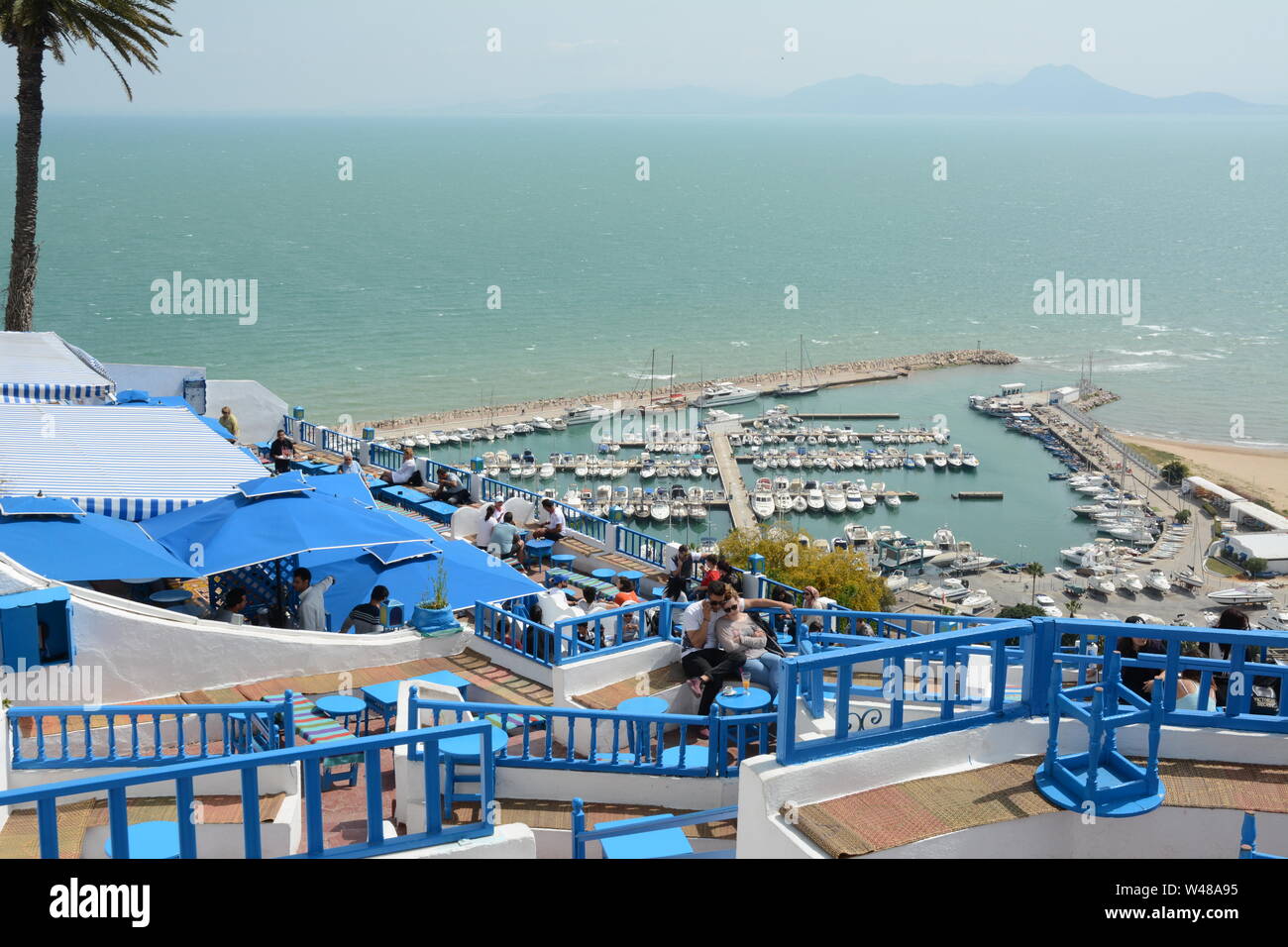 Una giovane coppia Tunsian sedersi a un tavolo del bar che si affaccia sulla acquamarina Mare Mediterraneo e il porto della città di Sidi Bou Said, Tunisi, Tunisia. Foto Stock