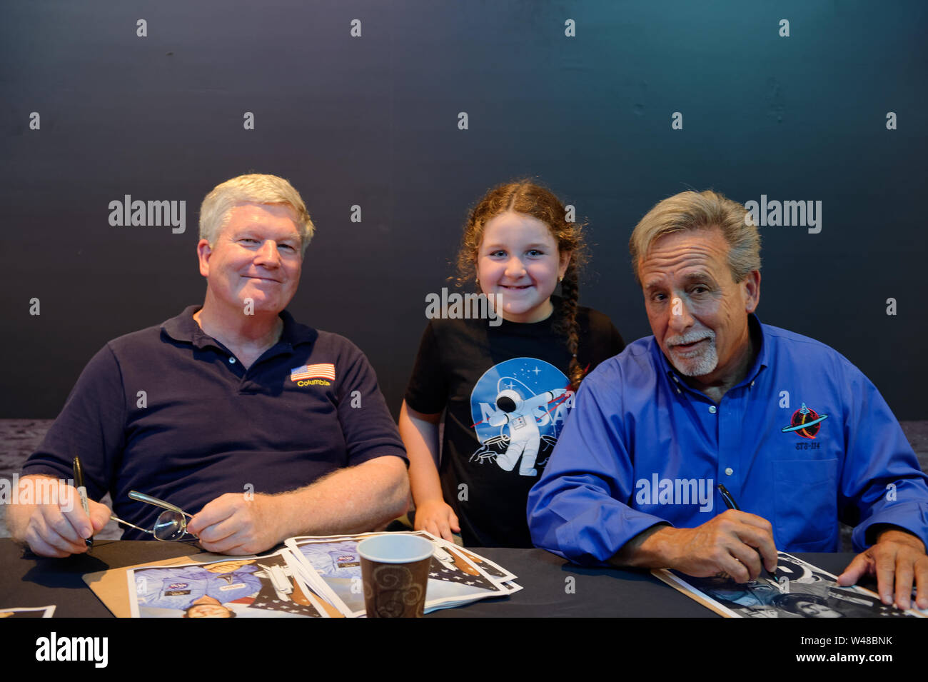 Città Giardino, New York, Stati Uniti d'America. Il 20 luglio, 2019. L-R, NASA Space Shuttle astronauta BILL PASTORE, ADRIANA IACONO, 6, di Franklin Square e lo Space Shuttle astronauta CHARLIE CAMARDA, sono presso l'astronauta autographing tabella, al Moon Fest Apollo a 50 celebrazione per il conto alla rovescia a culla di Aviation Museum di Long Island, durante il tempo in cui Apollo 11 Modulo Lunare, l'Aquila, sbarcati sulla luna 50 anni fa. Credito: Ann Parry/ZUMA filo/Alamy Live News Foto Stock