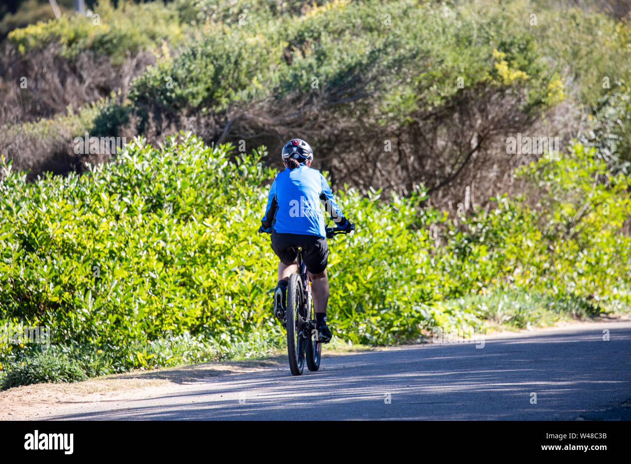 Donna australiana in abiti da bicicletta e casco in bicicletta che cavalcano la sua mountain bike attraverso la macchia, Sydney, Australia Foto Stock