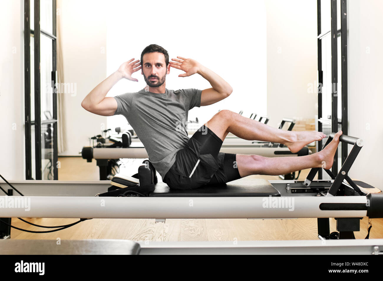 Uomo di eseguire un pilates Stretching di una gamba esercizio su un letto di reformer in una palestra la torsione e verso la telecamera di allungare e tonificare la muscolatura addominale Foto Stock