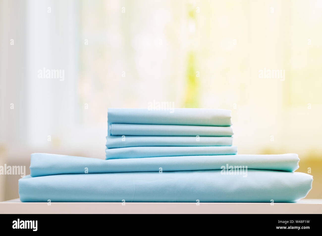 Close-up di blu biancheria da letto pulita su uno sfondo sfocato. Una pila di fogli piegati nuove lenzuola sul tavolo. La luce del sole dalla finestra. Foto Stock