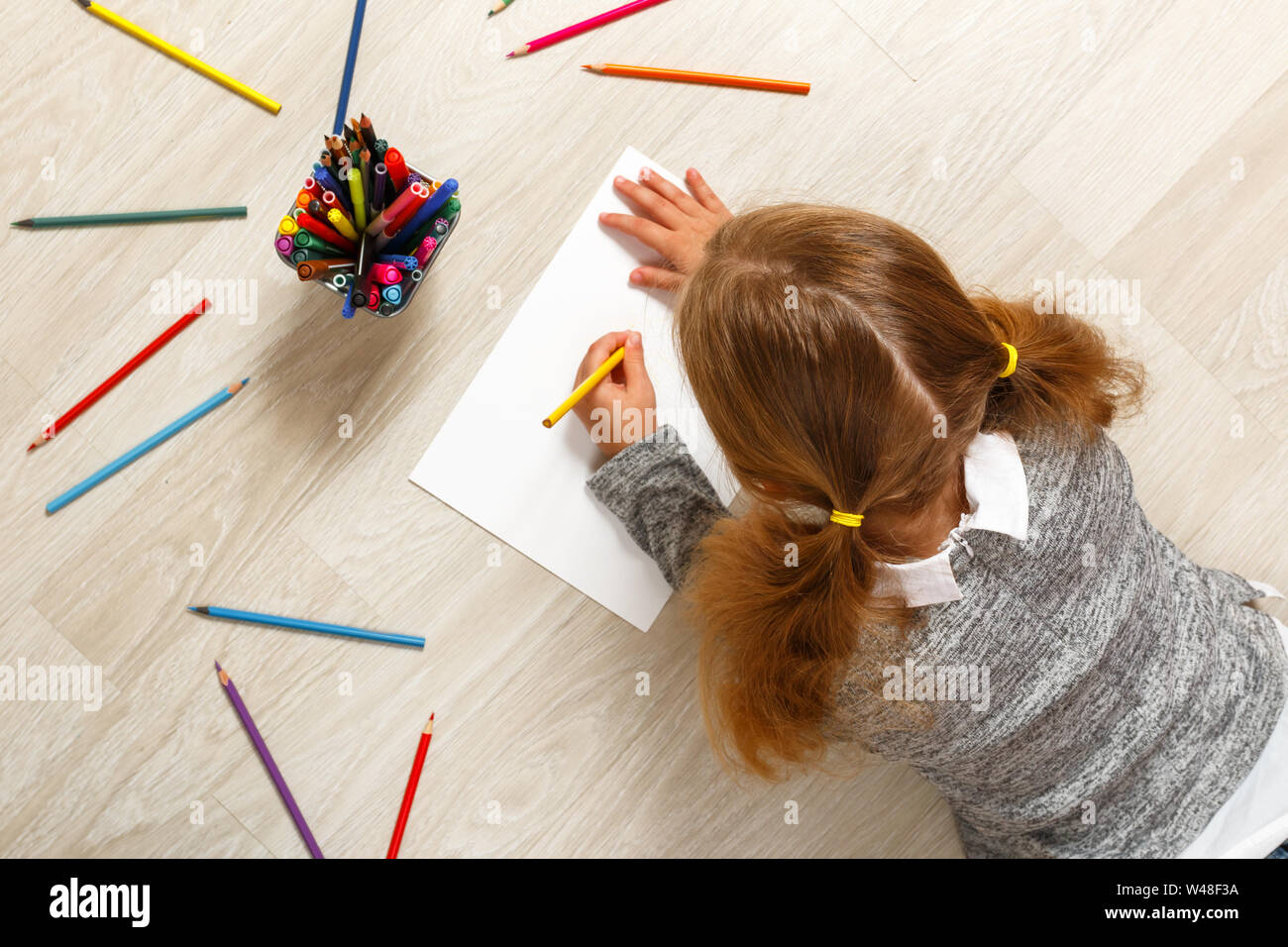 Vista dall'alto di una bambina che giace e pittura sul pavimento nella sua stanza in casa. Foto Stock