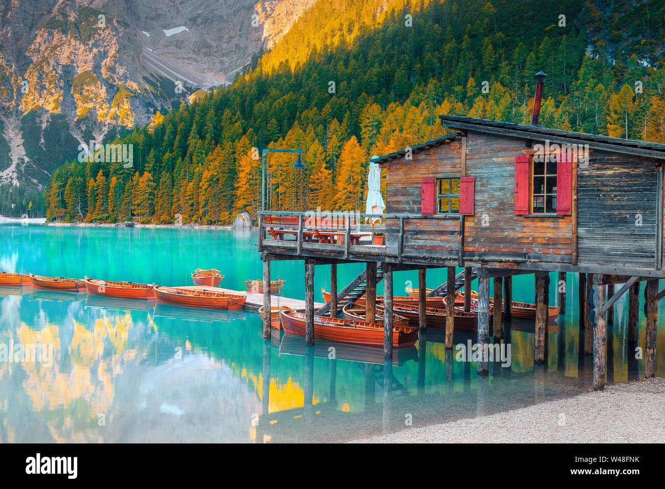 Il pittoresco lago alpino e il bellissimo paesaggio autunnale con giallo larici. Popolare destinazione turistica con barche di legno e legno carino boathouse, Foto Stock