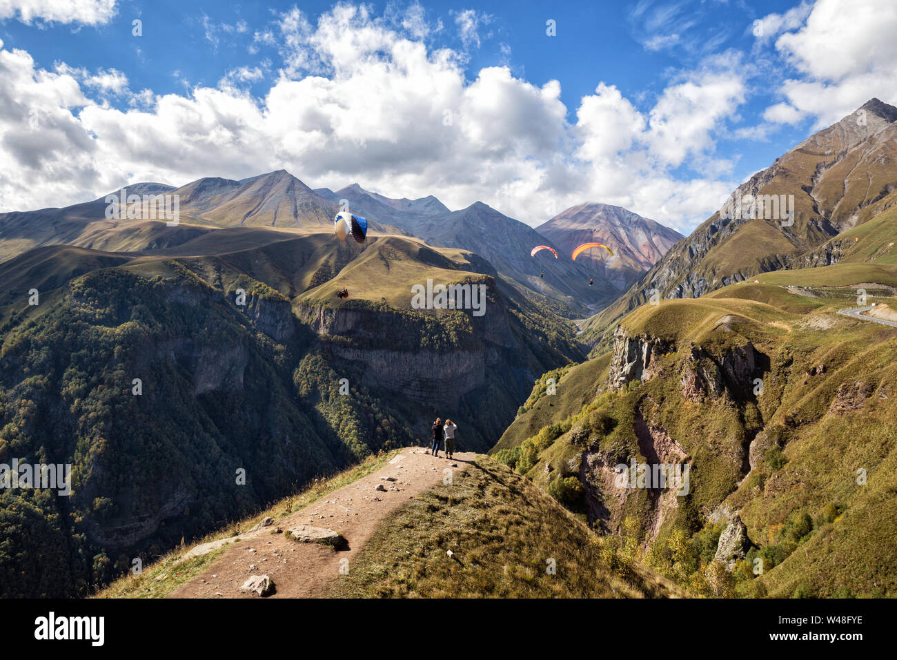 Scenic paesaggio di montagna. Due donne turisti scattare foto come parapendii sorvolare Gorge, il Caucaso, Georgiano strada militare, Georgia Foto Stock