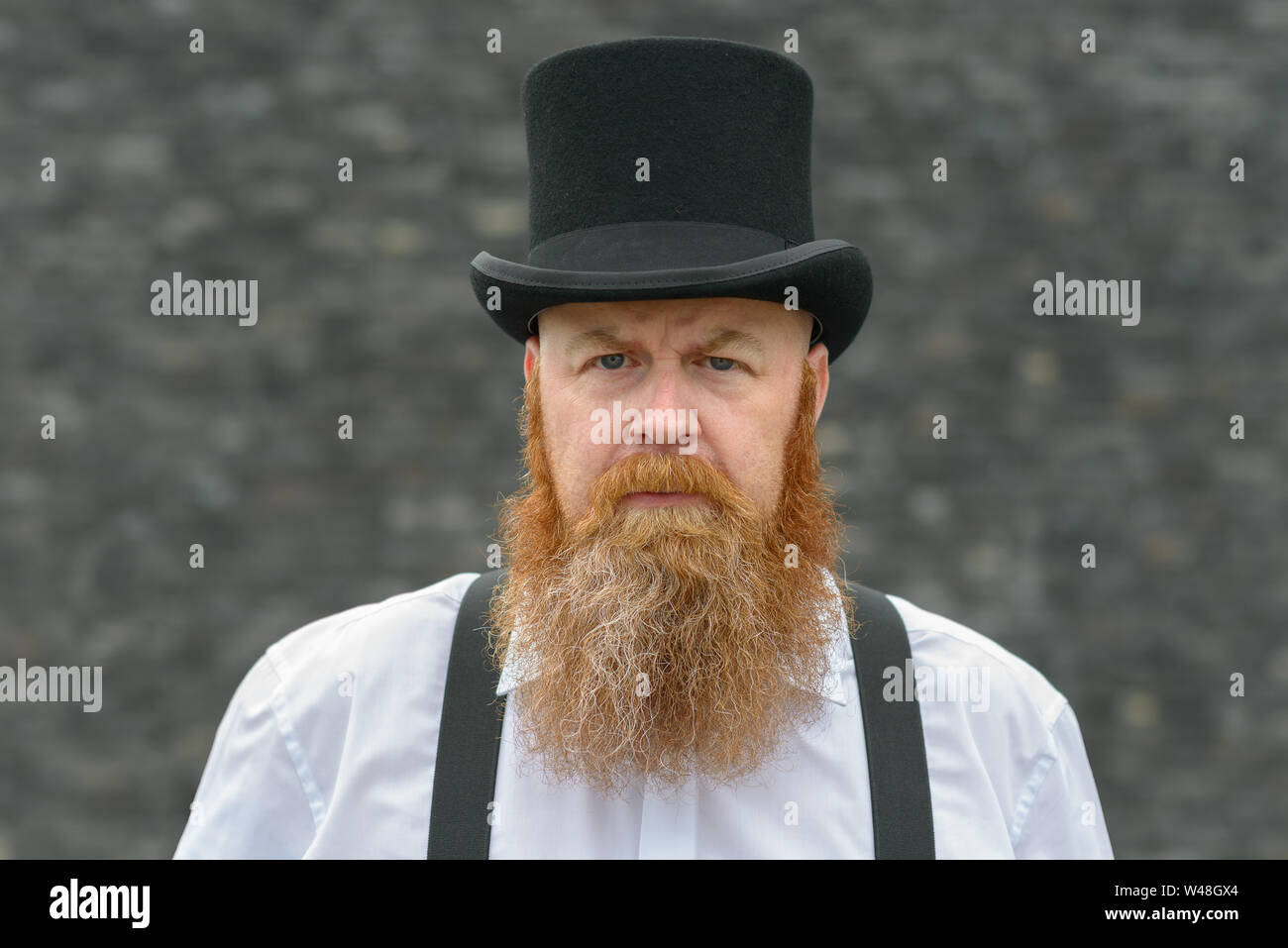 Intensa l'uomo serio indossare top hat e bretelle fissando la telecamera con uno sguardo penetrante e preoccupato cipiglio Foto Stock