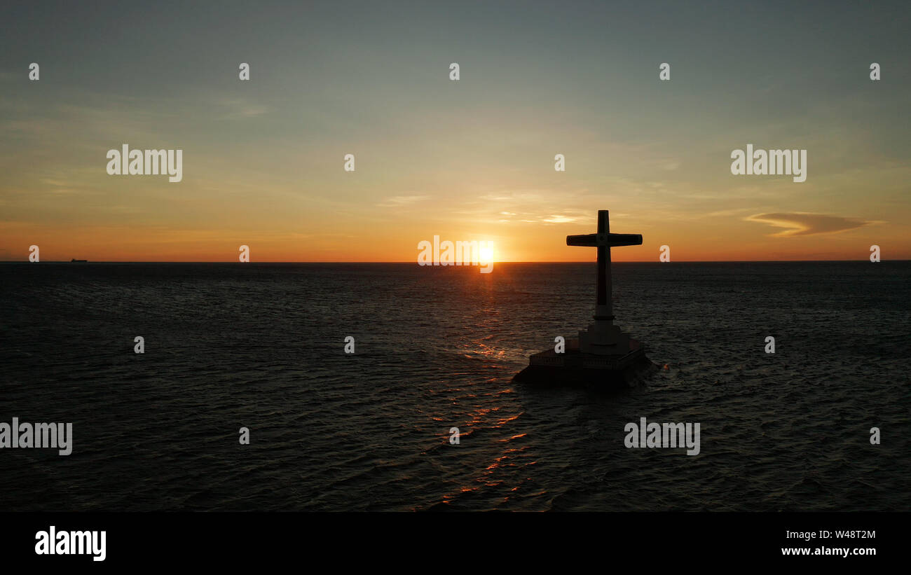 Croce cattolica nel cimitero affondata nel mare al tramonto, Vista aerea. Colorato nubi luminose durante il tramonto sul mare. Tramonto al cimitero affondata Camiguin Island Filippine. Foto Stock