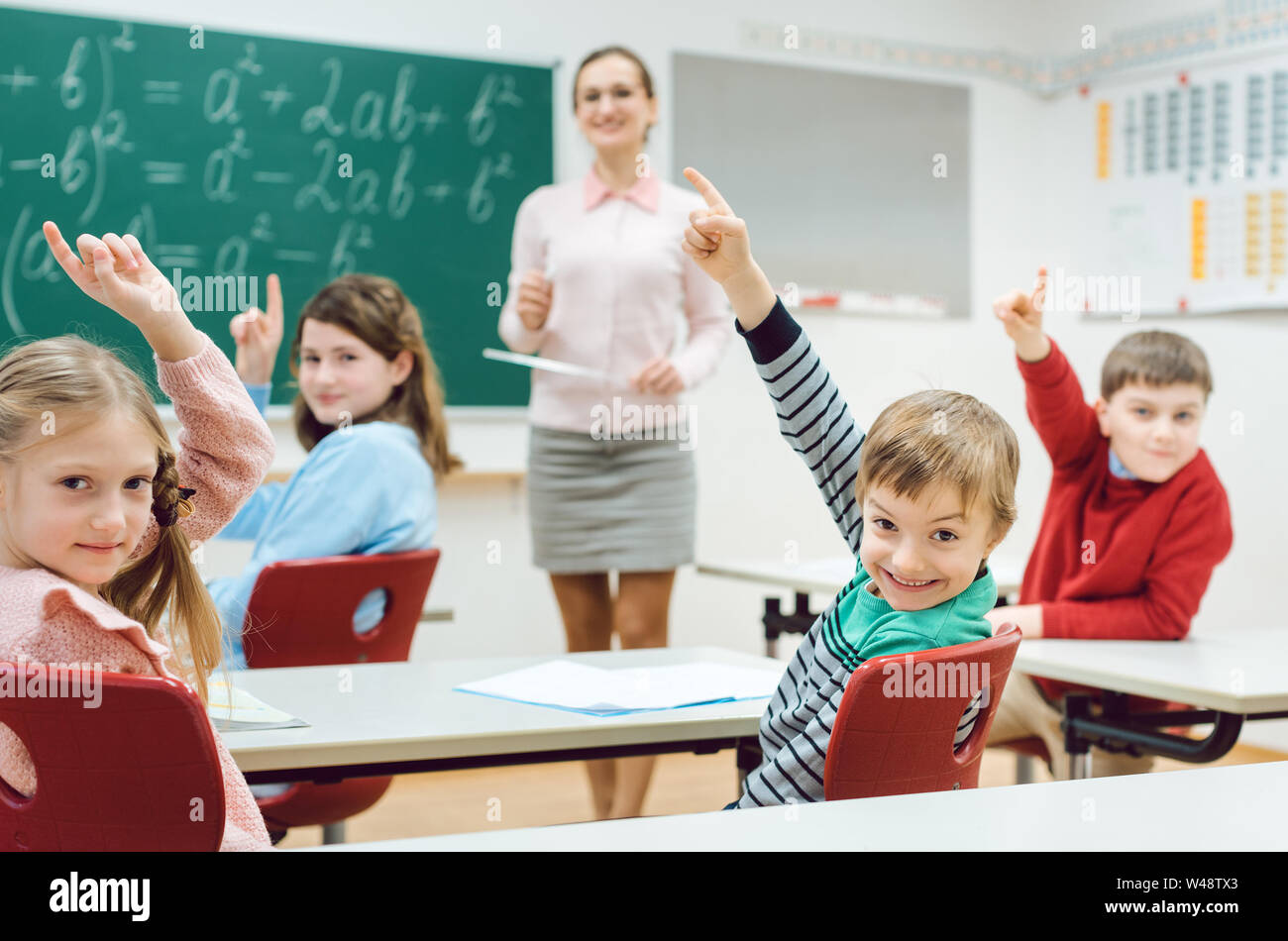 Gli studenti nella classe alzando le mani per rispondere a una domanda Foto Stock