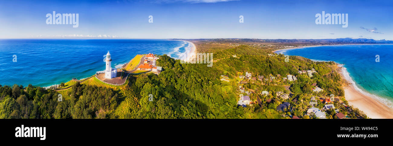 In alto di capezzagna con Byron Bay lighthouse alta sopra la costa dell'oceano Pacifico in una giornata di sole in elevata panorama antenna rivolta verso l'interno sopra le spiagge sabbiose. Foto Stock