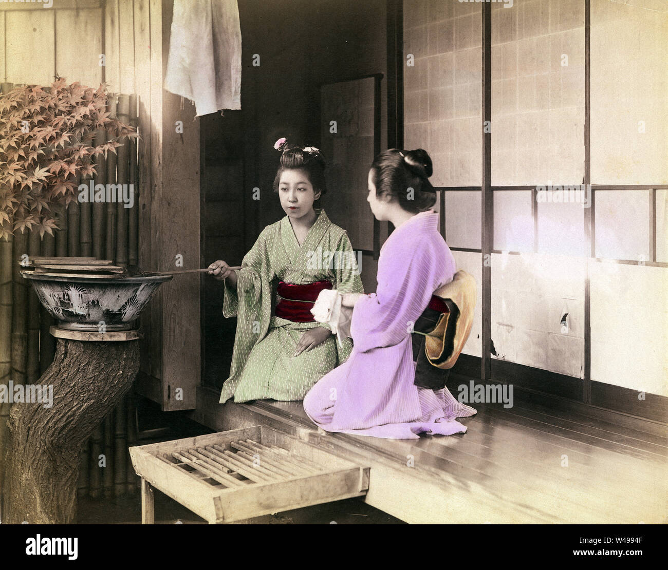 [ 1890 Giappone - Le donne giapponesi lavaggio delle mani ] - una donna in kimono utilizza un Hishaku (siviera) per spruzzare acqua sulle mani di un'altra donna che sta lavando le mani. Le due ragazze sono seduti sulla veranda di una casa privata. Lavaggio delle mani (Temizu) è un importante rituale di purificazione durante l'inserimento di sacrario scintoista motivi, ma è stato anche fatto al momento di entrare in una casa privata. Xix secolo albume vintage fotografia. Foto Stock