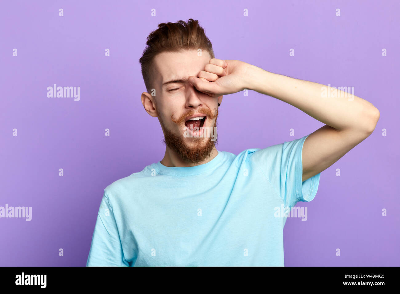 Bella annoiato assonnato uomo barbuto di toccare gli occhi dopo un lungo periodo di superlavoro sul nuovo progetto, vuole dormire al mattino, close up ritratto. isolato blu Foto Stock