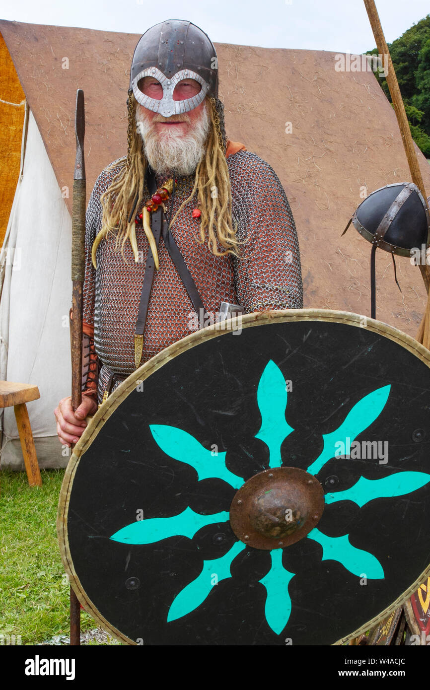 Età vichinga, costumi di abbigliamento e armi a Heysham, Lancashire. Luglio, 2019. Le bandiere di battaglia volano alla baia di Morecambe mentre 70 re-enactors del guerriero di eredità storica si riuniscono ad un'accampamento di storia vivente medievale per dimostrare le armi dell'era e fanno la battaglia sul verde del villaggio. Gli dei Idin, Thor e Frey furono celebrati insieme ad altre mitologie vichinghe. Foto Stock