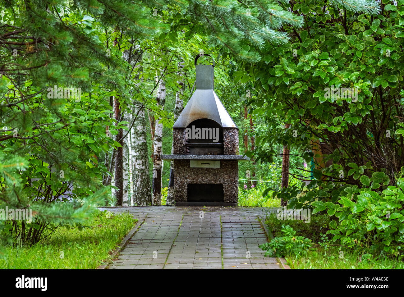 Braciere-forno per friggere la carne sulla griglia sullo sfondo di cespugli verdi. Foto Stock