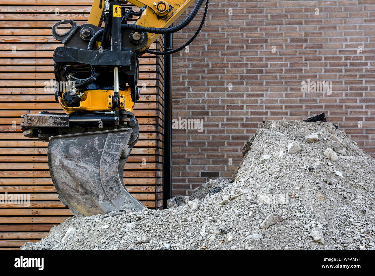 Benna di ferro dell'escavatore su un mucchio di ghiaia contro lo sfondo di un muro di mattoni Foto Stock
