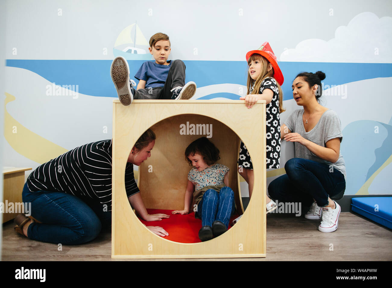 Tre bambini e due insegnanti interagiscono con un cubo di grandi dimensioni Foto Stock