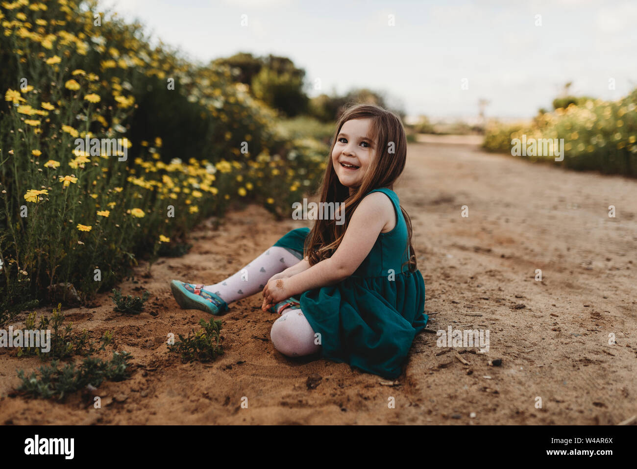 Bambina giocando in un campo di fiori con cielo blu dietro di lei Foto Stock