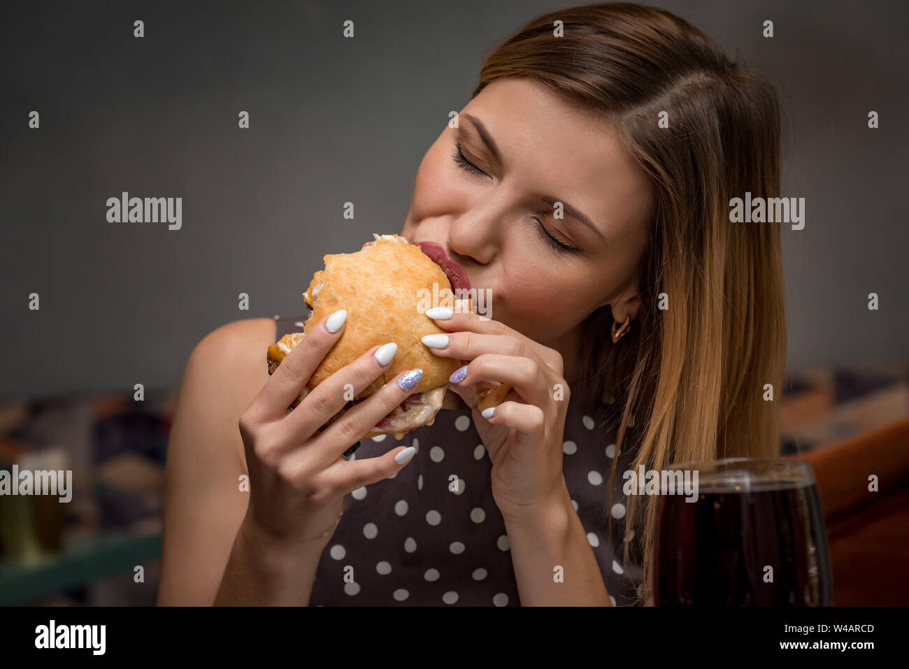 Giovane donna di mangiare hamburger in un ristorante. Close up viso con gli occhi chiusi Foto Stock