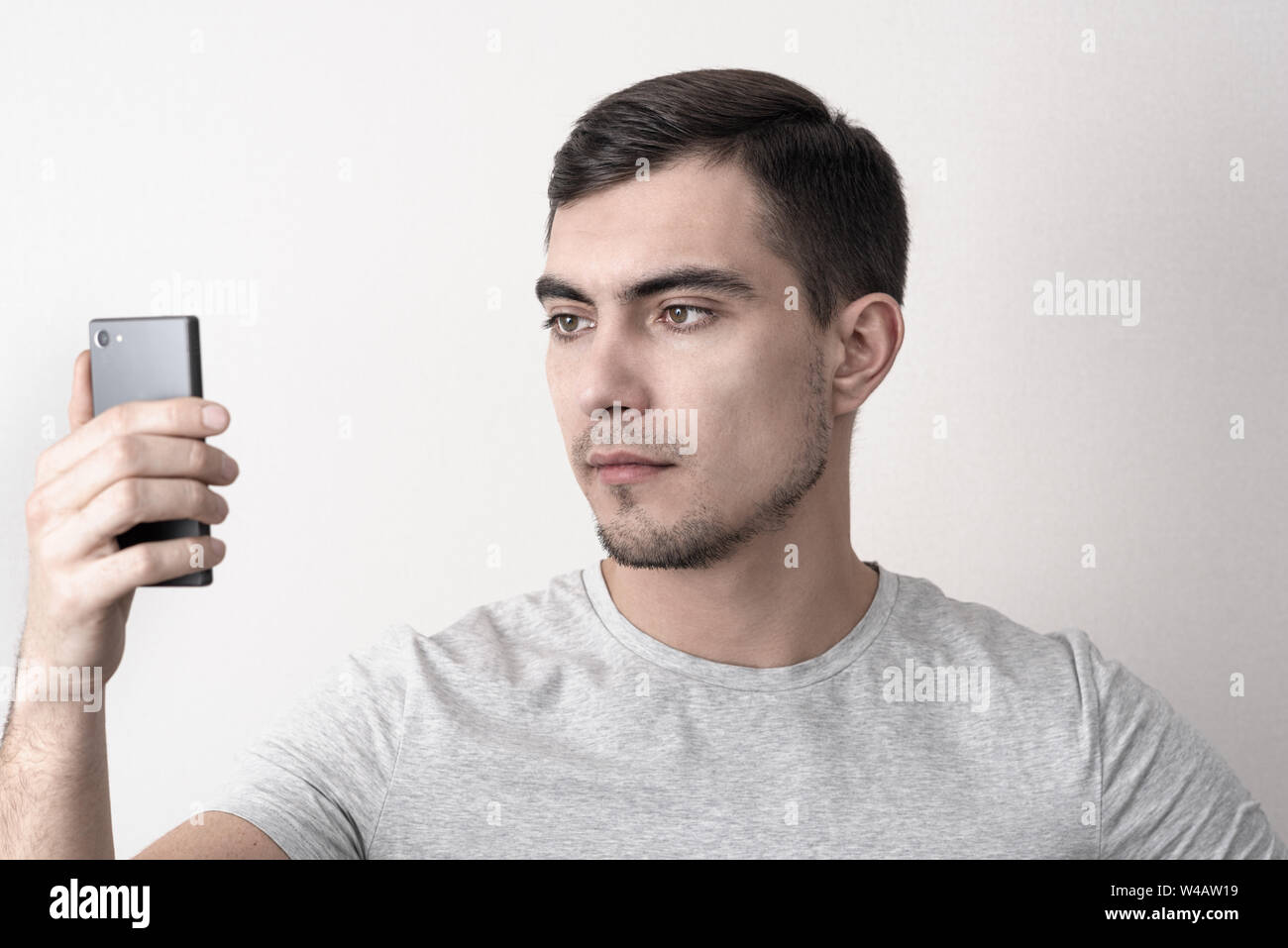 Uomo caucasico in grigio di t-shirt e smartphone in mano utilizza il riconoscimento del volto Foto Stock