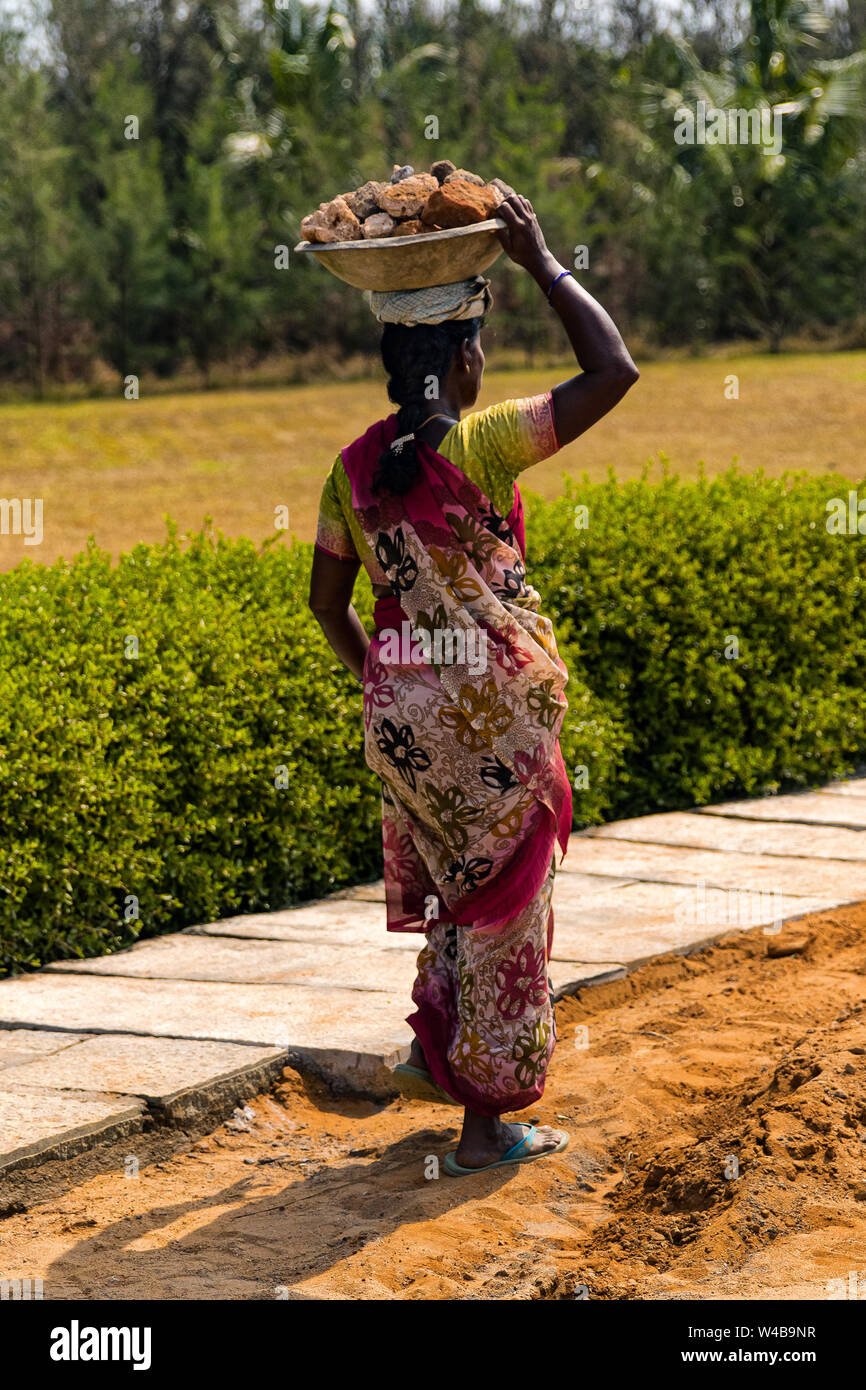 Donna indiana esecuzione di duro lavoro manuale di rocce di clearing, bilanciamento sulla sua testa. Foto Stock