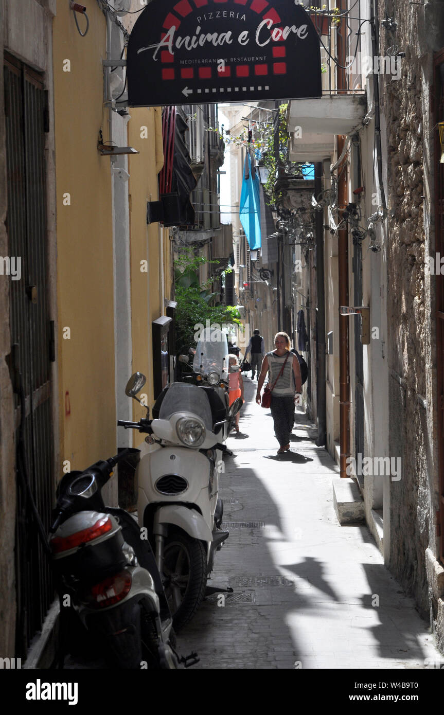 Una tipica stradina nel Ortegia, con balconi, pizzerie, gente camminare, e moto o scooter parcheggiate ovunque. Foto Stock