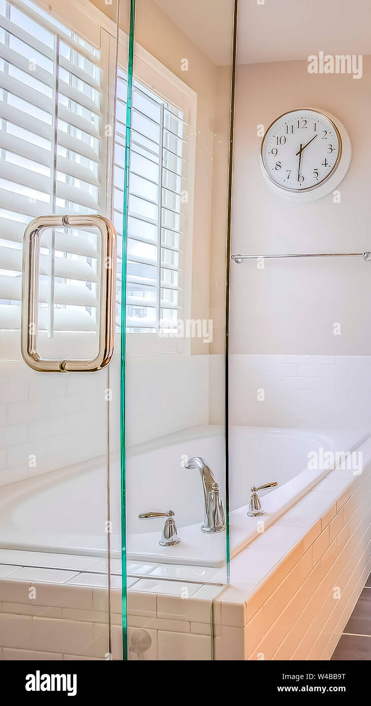 Altezza verticale bagno interno con costruito nella vasca da bagno doccia e  area vanity. Una camera da letto e finestra con persiane possono essere  viste attraverso la porta aperta Foto stock -