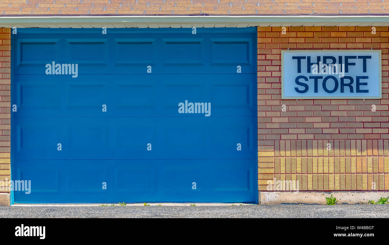 Panorama edificio con tetto spiovente e grande porta blu visualizzati in una giornata di sole. Una parsimonia Store segno si blocca sul mattone parete esterna dell'edificio. Foto Stock