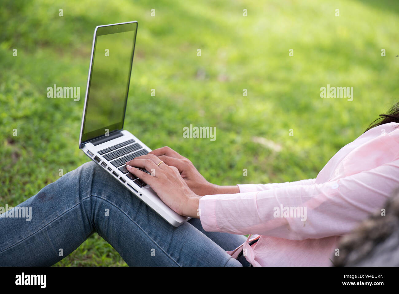 Giovane bella donna che lavorano all'esterno in un parco pubblico. Lavorando su laptop all'esterno. Immagine ritagliata del lavoro femminile su laptop mentre è seduto in un parco. Foto Stock