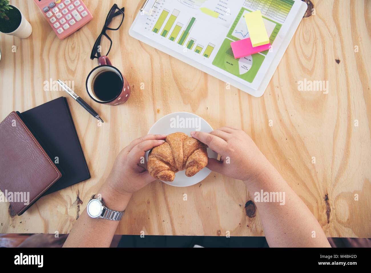 Chubby donna grassa hanno una colazione sulla scrivania. Croissant e caffè. Foto Stock