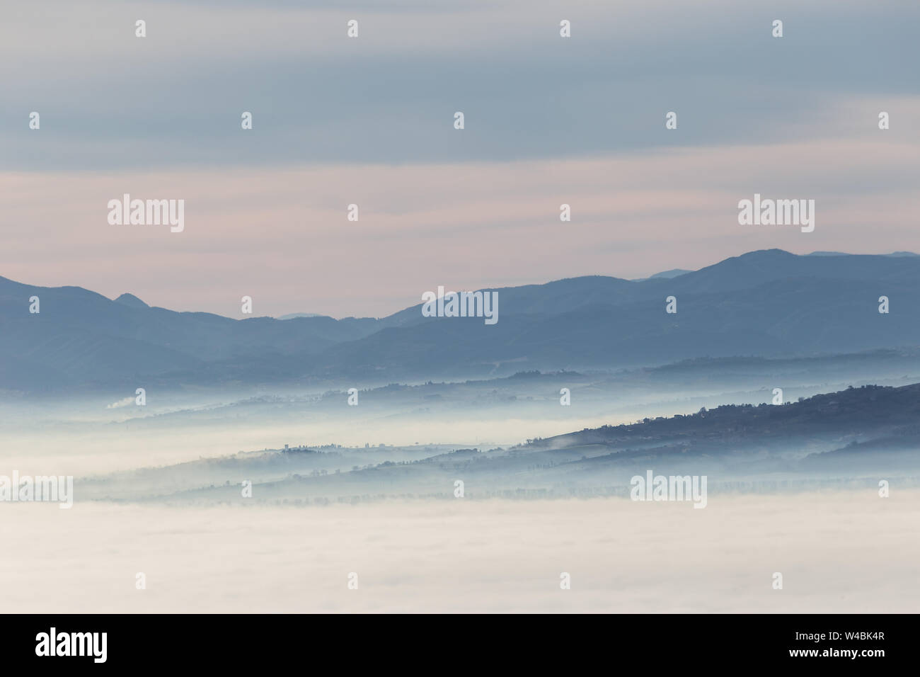 La nebbia di riempimento di una valle in Umbria (Italia) all'alba, con strati di montagne e colline e varie sfumature di blu Foto Stock
