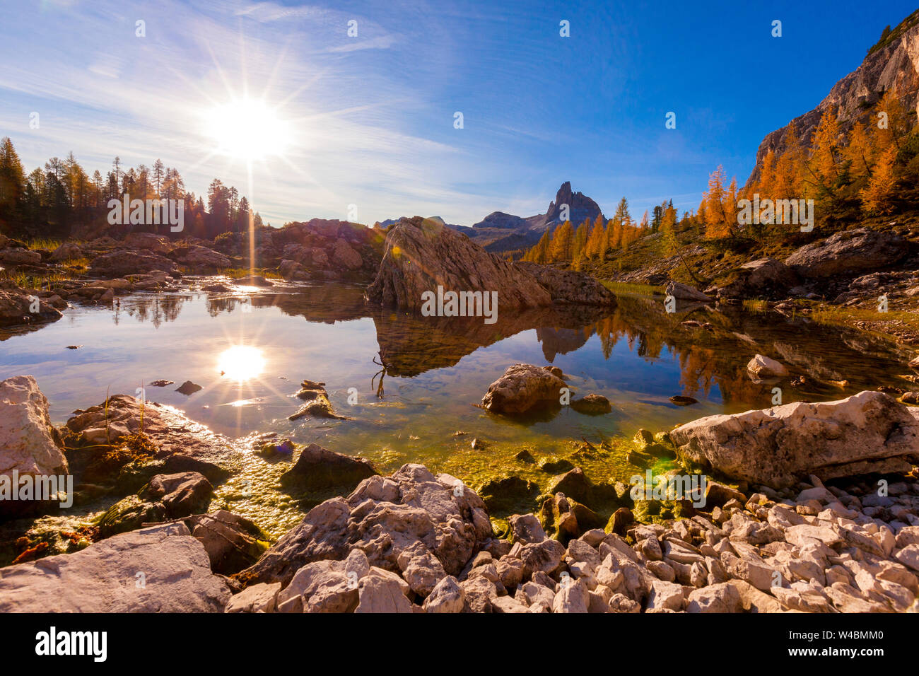 Sunburst sul lago Federa e Becco di Mezzodi circondato da pini larici in autunno, Dolomiti, Cortina d'Ampezzo, Veneto, Italia Foto Stock