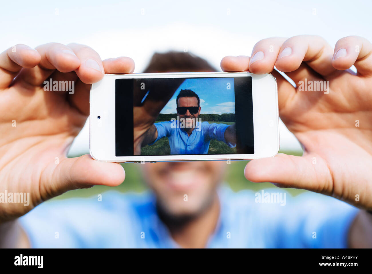 Foto di un giovane uomo sorridente prendendo un selfie con il suo cellulare Foto Stock