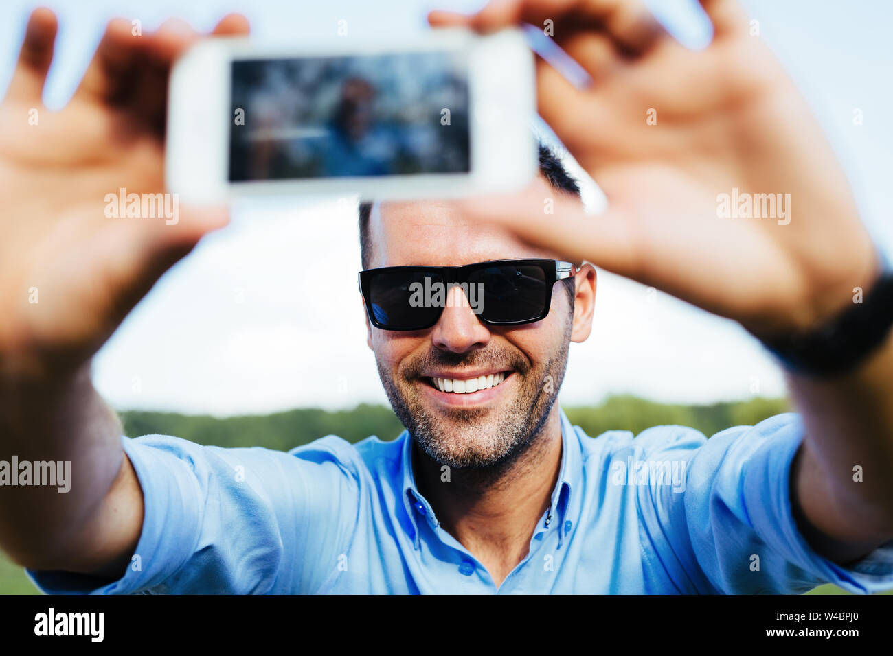 Ritratto di un bel uomo felice prendendo un selfie all'aperto con il suo smartphone Foto Stock