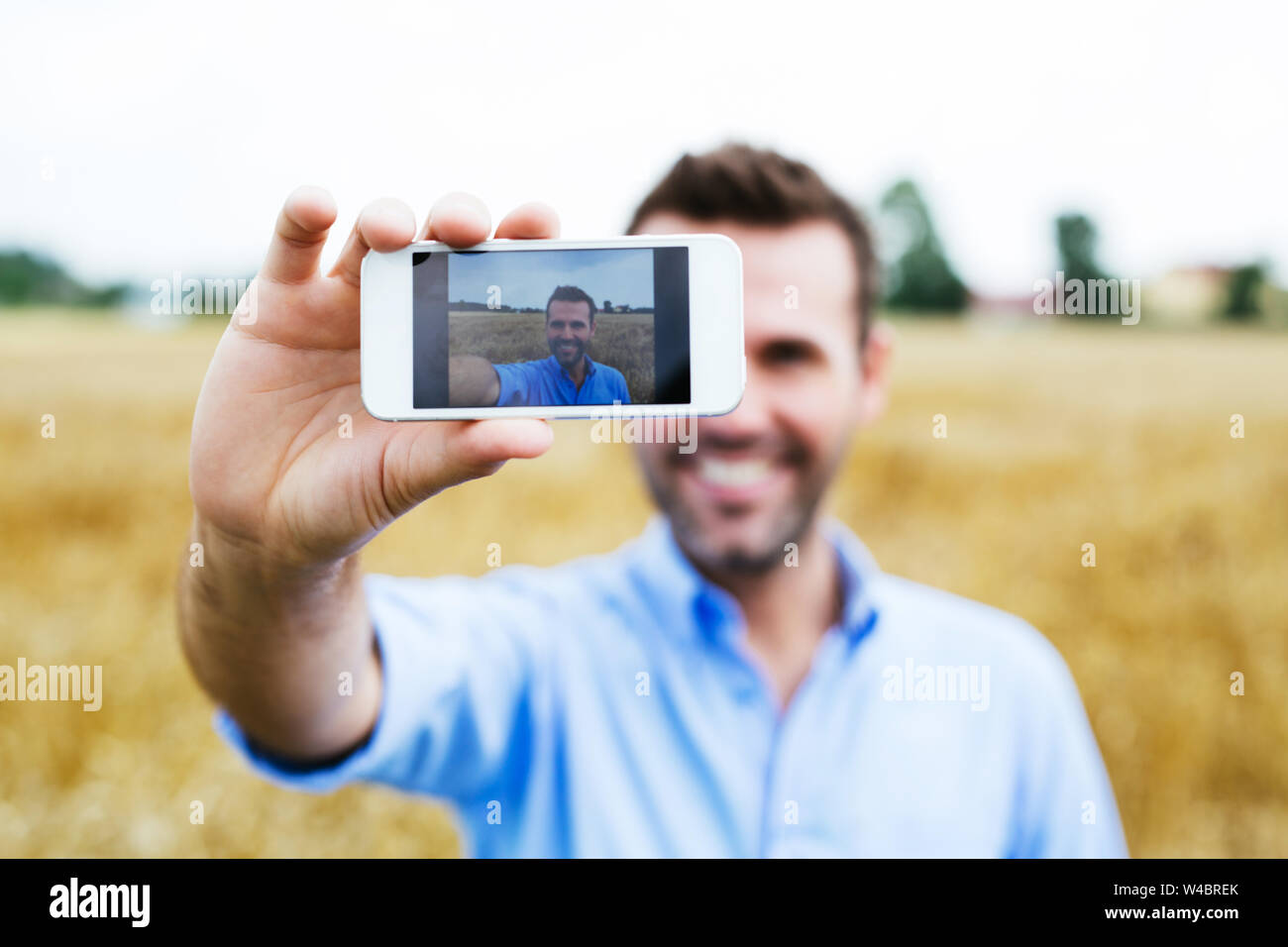 Felice l'uomo prendendo selfie in un campo, sfondo sfocato Foto Stock