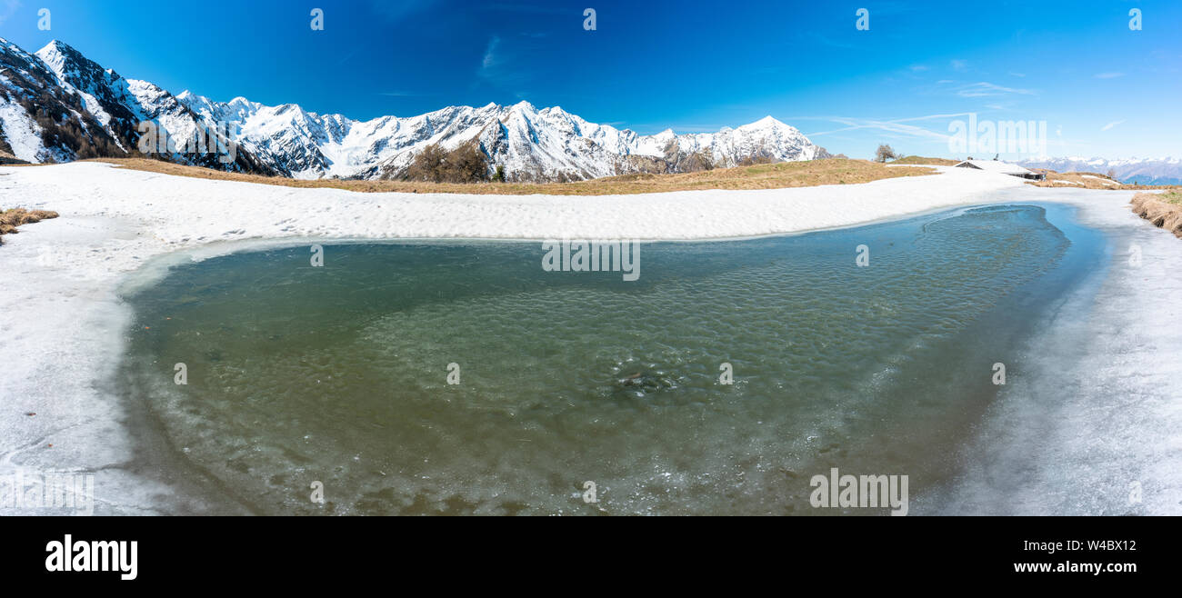 Panoramica del Monte Legnone e fusione del ghiaccio presso l'Alpe Piazza durante la primavera del disgelo, Val Gerola, Valtellina, Lombardia, Italia Foto Stock