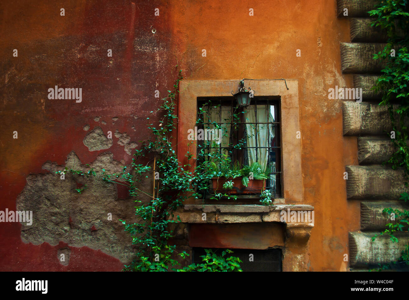 Uno vintage lanterna di ferro su una finestra su un arancione e parete rossa. Piante verdi in un vaso di fiori su un davanzale intrecciano con piante verdi in città ce Foto Stock