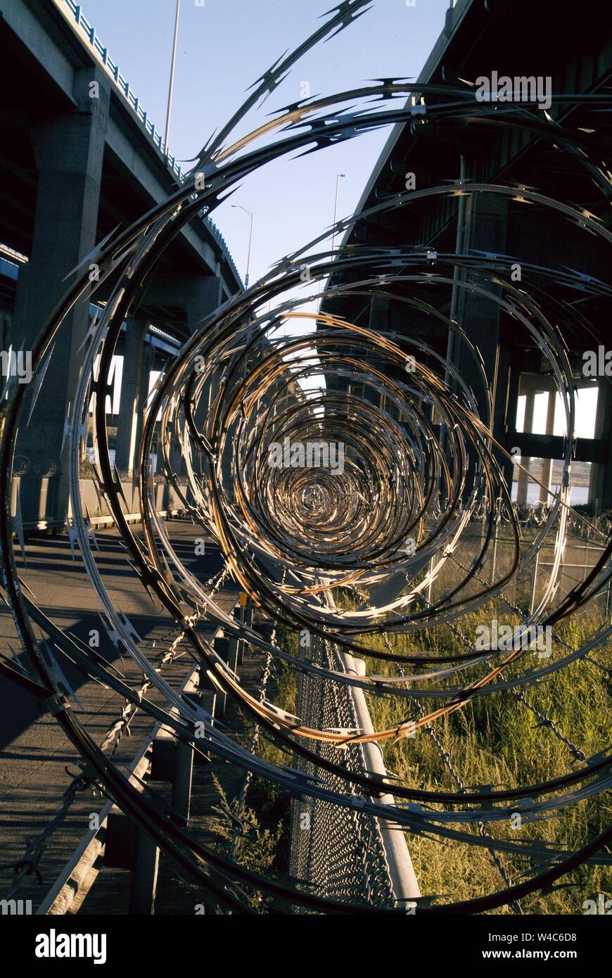 BLOCCO: Spirali di filo spinato lungo la cima di una recinzione in un complesso industriale sotto una strada sopraelevata a Perth Amboy, New Jersey. Foto Stock
