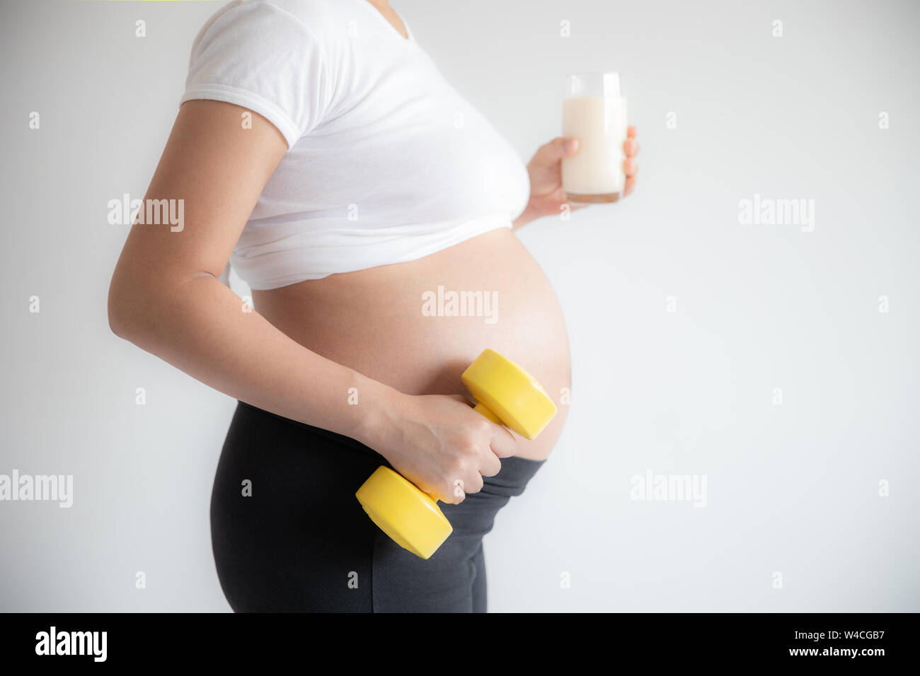 donna incinta e pesi dumbbell esercizio di formazione con un bicchiere di latte Foto Stock