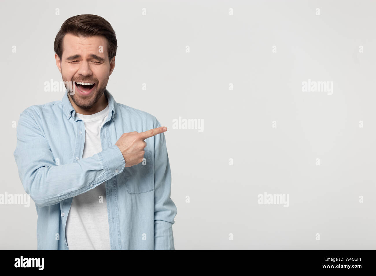 Sogghignando guy puntare il dito a copyspace isolato su sfondo grigio Foto Stock