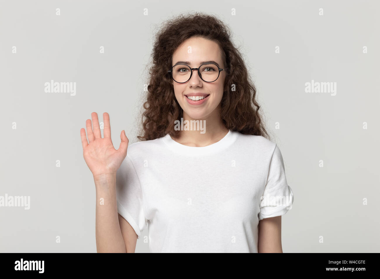 Ragazza sorridente in bicchieri guardando la telecamera a mano d'onda studioshot Foto Stock