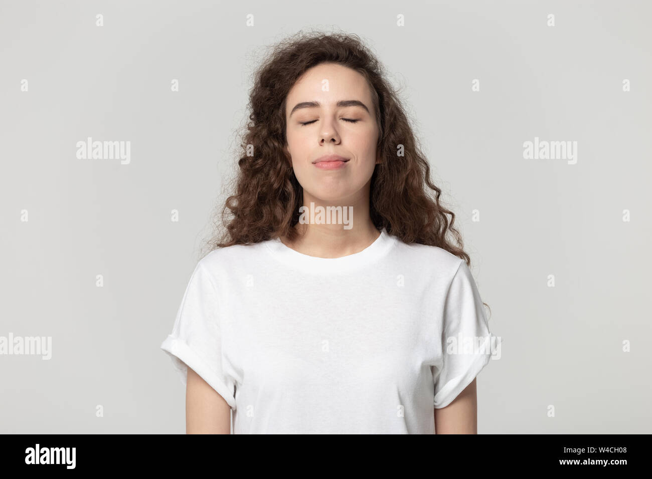 La donna gli occhi chiusi godere di aria fresca pongono isolato su grigio Foto Stock