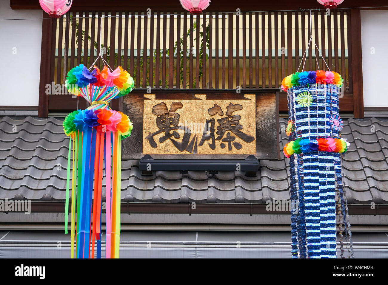 Le festive colorate (colorate) streamers si trovano davanti al tetto di piastrelle nere di un ristorante e firmano la celebrazione di Tanabata in Giappone. Foto Stock
