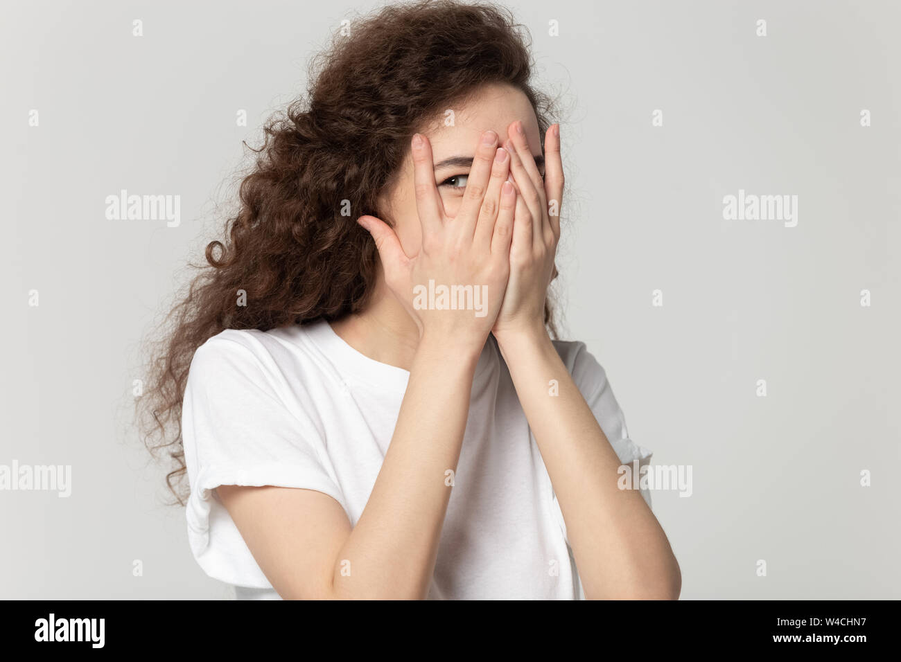 Sly ragazza faccia nascondere dietro le mani pigoli attraverso le dita Foto Stock