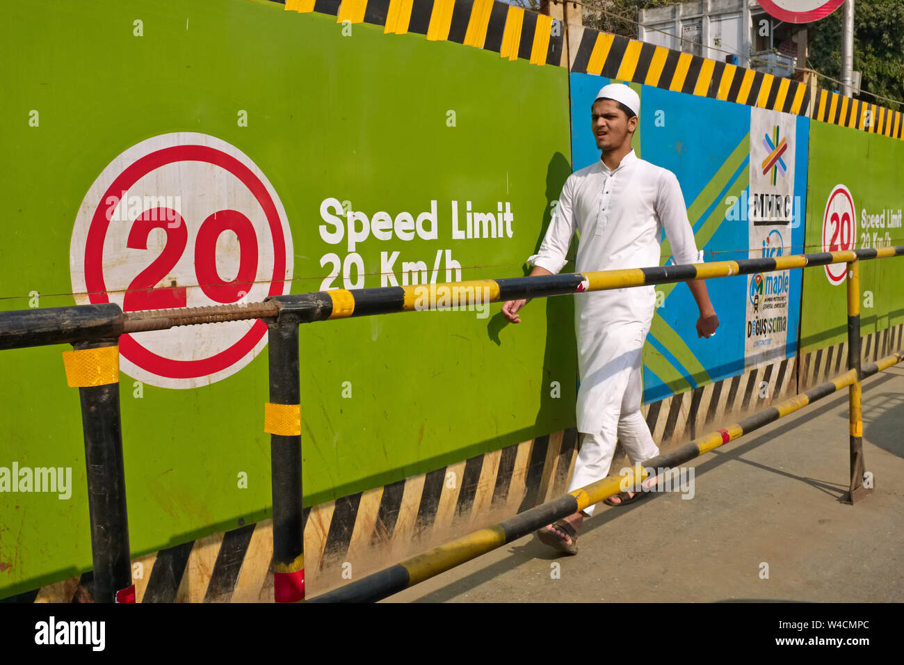 Un pedone che indossa un cappello musulmano passando la recinzione di un cantiere per un nuovo percorso della metropolitana di Mumbai, Mumbai, India Foto Stock