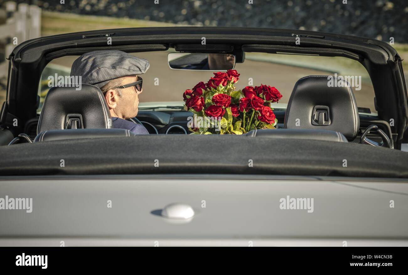 Maschio caucasico nella sua 60s con il mazzo di rose rosse per andare per una data alla guida del suo nuovo convertibile auto moderne. Foto Stock