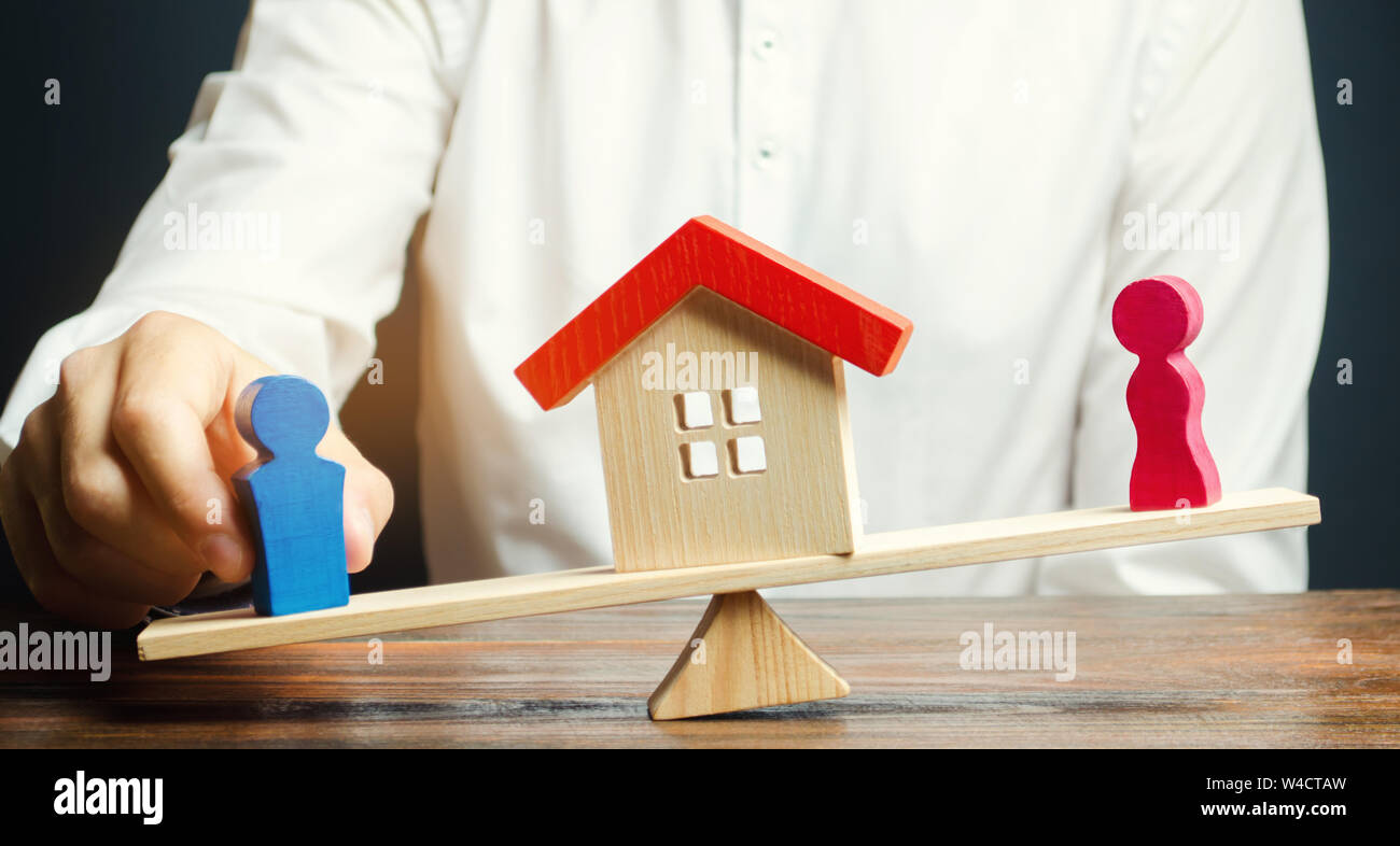 Figure in legno di un uomo e di una donna su una bilancia e una casa tra loro. Divisione della proprietà mediante mezzi legali. Il chiarimento di proprietà dell'alloggiamento Foto Stock
