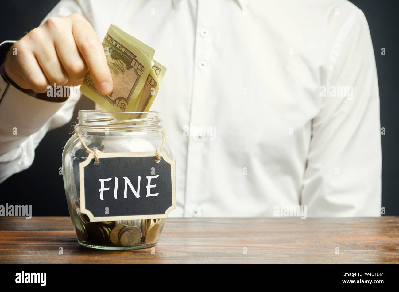 Un uomo mette dollari in un vasetto di vetro con la parola fine. Risparmio di denaro e di pagare una multa. La punizione per un crimine e reato. Pene finanziarie. Violat Foto Stock