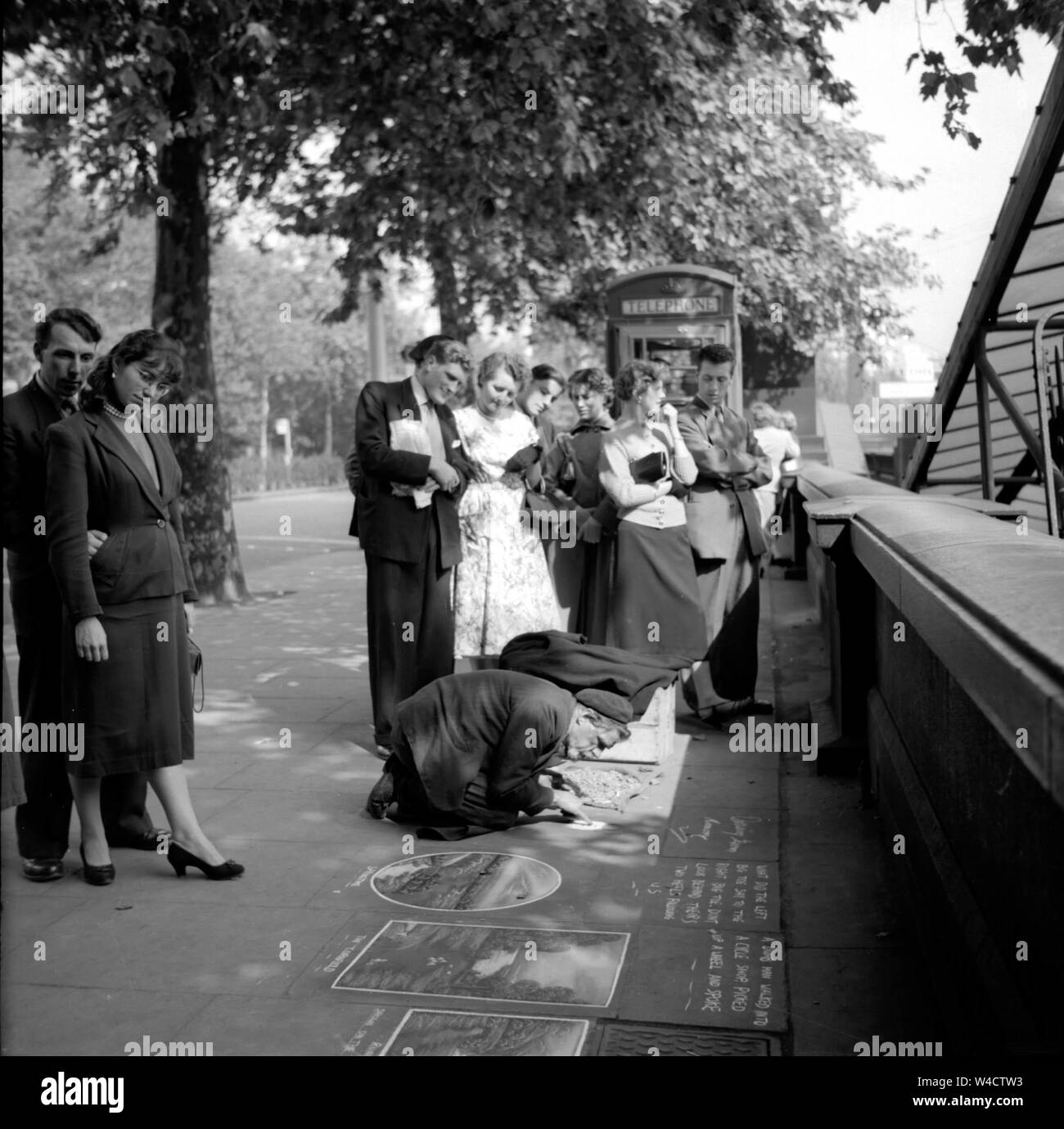 Un'annata di scena sul terrapieno a Londra come una folla si raduna attorno a un marciapiede artista al lavoro con il suo chalk negli anni cinquanta Foto Stock