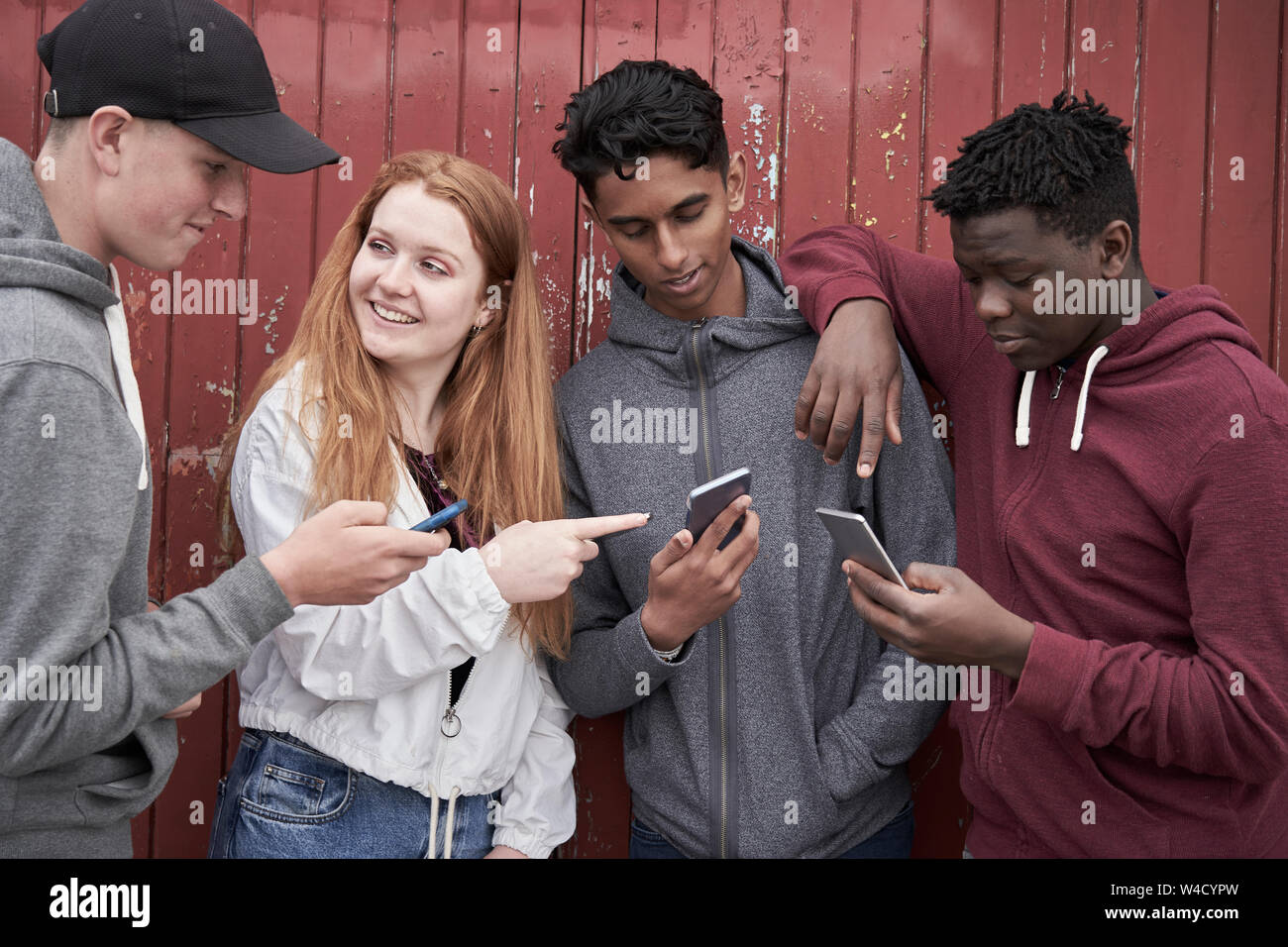 Gruppo di amici adolescenti guardando i telefoni cellulari nel contesto urbano Foto Stock