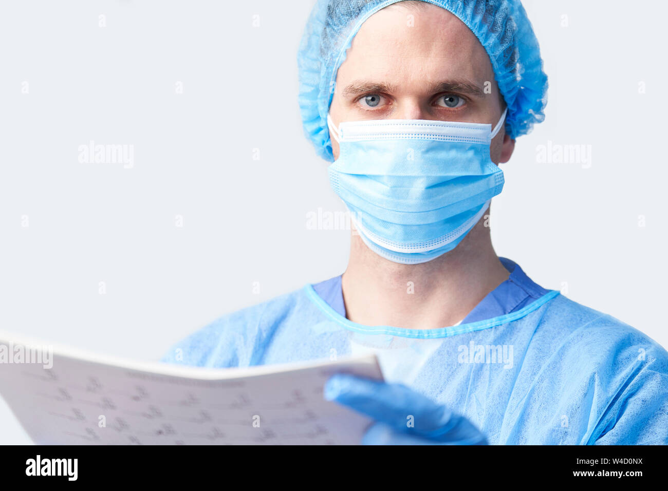 Ritratto in studio di chirurgo maschio indossando camice e maschera Holding Medical Stampare Foto Stock