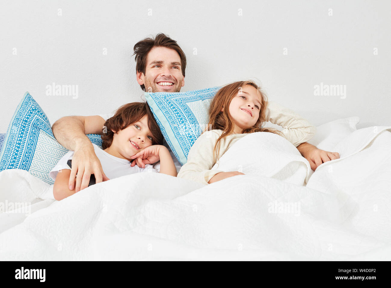 Padre Felice e i due ragazzi insieme guardare la TV a letto Foto Stock