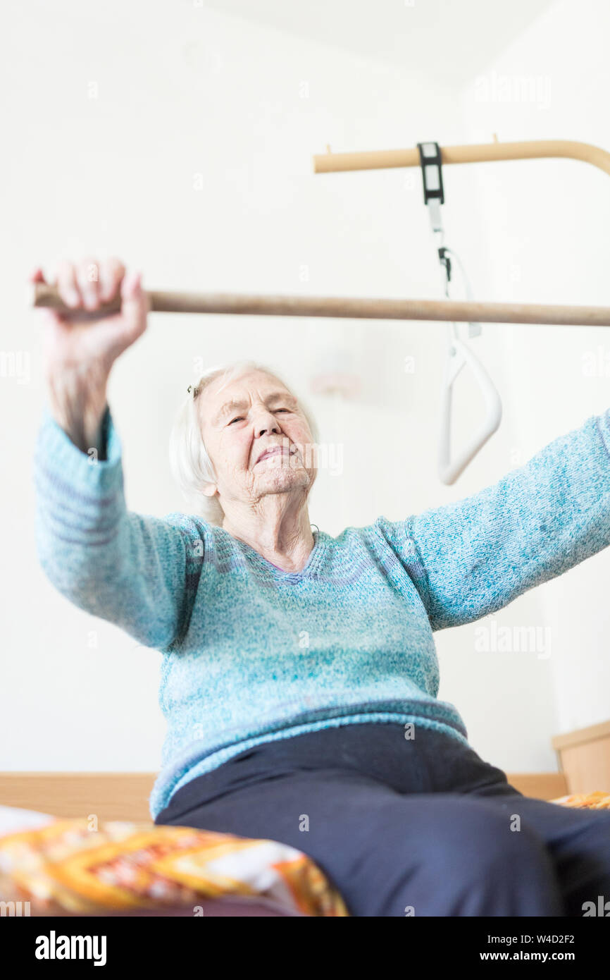 Anziani 96 anni vecchia donna esercizio con un bastone seduta sul suo cattivo. Foto Stock